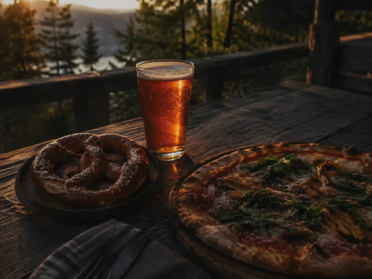 A soft pretzel, thin crust pizza, and a pint of amber beer on the Depot's pine-shaded deck at golden hour